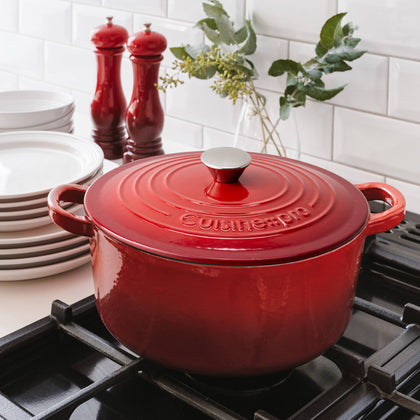 Cuisine::pro® LE CONNOISSEUR™ 6.6 Qt. Round French Oven in red on a stove with plates in the background.