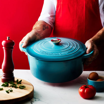 Cuisine::pro® LE CONNOISSEUR™ 6.6 Qt. Round French Oven in a vibrant blue held by a chef.