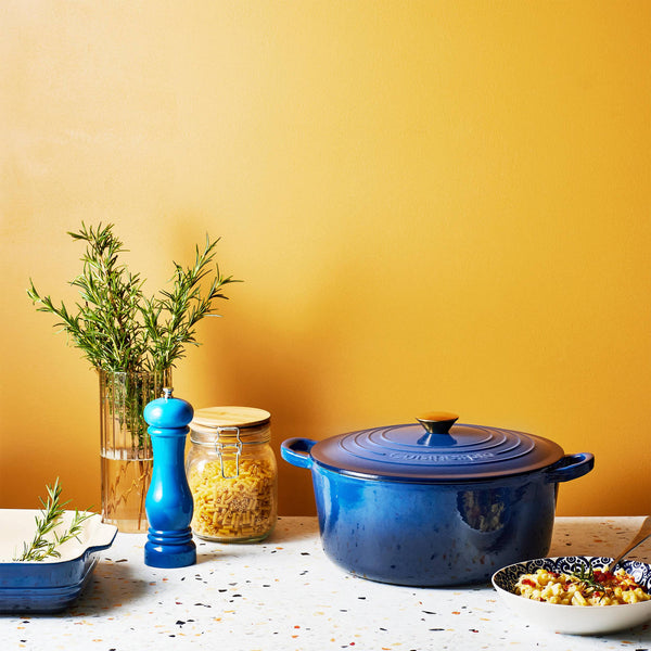 Cuisine::pro® LE CONNOISSEUR™ 6.6 Qt. Round French Oven in blue with cooking ingredients on a kitchen table.