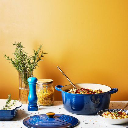 Cuisine::pro® LE CONNOISSEUR™ 6.6 Qt. Round French Oven with hearty meal and herbs on table.